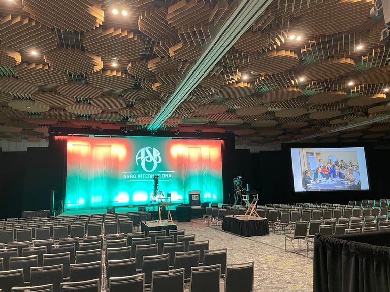 Empty auditorium with rows of grey chairs facing a stage with large LED screens and blue light beam