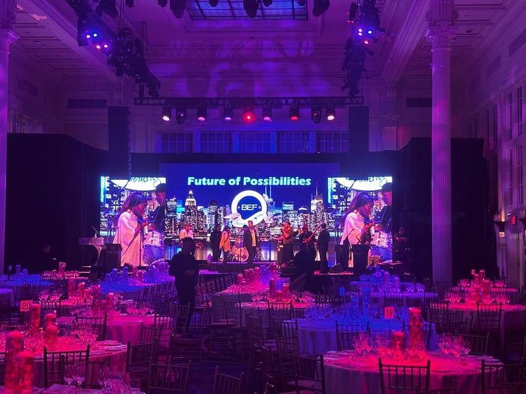 Large event venue with purple and blue stage lighting, Future of Possibilities text on screens and red-lit dining tables