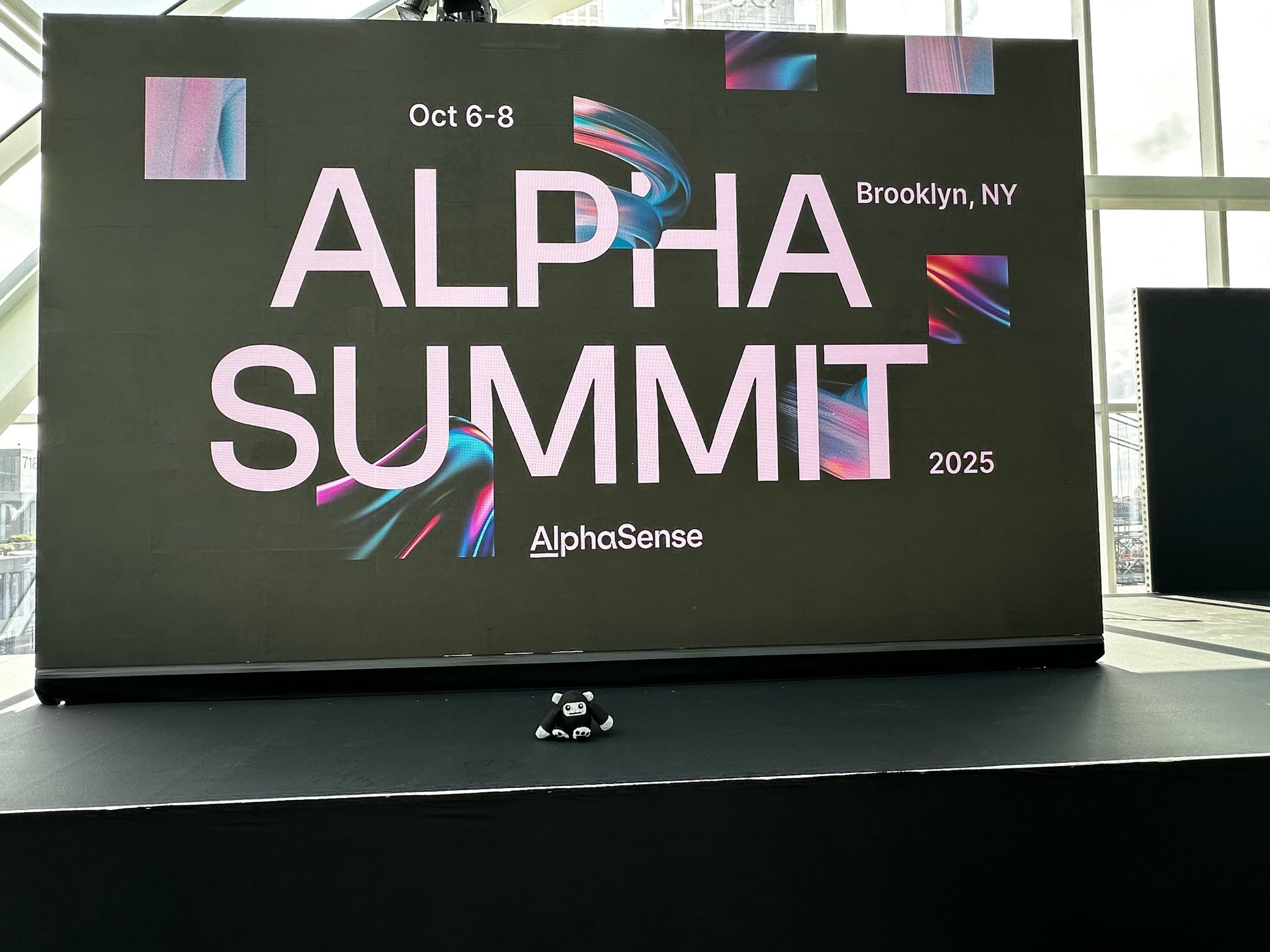 Alpha Summit 2025 promotional display screen showing event dates Oct 6-8 in Brooklyn, NY